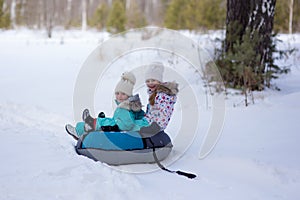 Joyful girls ride a tubing from a hill together. Winter holiday