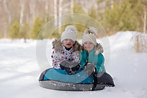 Joyful girls ride a tubing from a hill together. Winter holiday