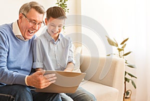 Joyful Grandfather And Boy Using Laptop Laughing Sitting At Home