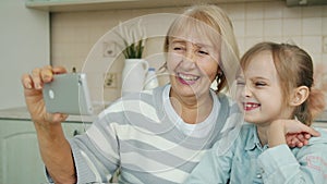 Joyful granny and little girl taking selfie with smartphone camera in cozy modern kitchen