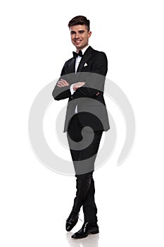 Joyful groom standing with arms and legs crossed