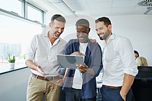 Joyful group of colleagues in office laughs looking at tablet