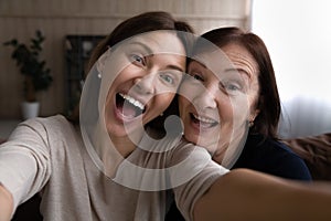 Joyful grown daughter taking funny selfie together with retired mother