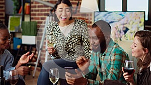 Joyful guests in living room reacting to online clips on mobile phone