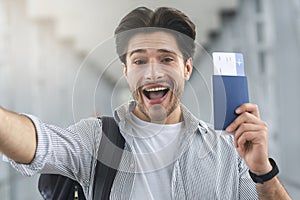 Joyful guy taking selfie with passport and poarding passes in airport
