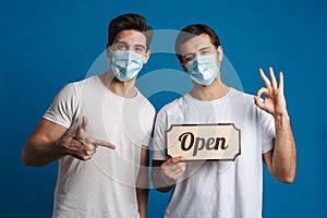 Joyful guys in protective masks gesturing while showing open sign board