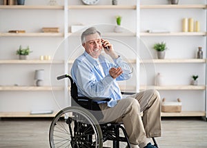 Joyful handicapped senior man in wheelchair taking on smartphone at retirement home
