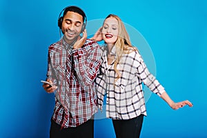 Joyful handsome man listening to music in headphones with closed eyes on blue background. Pretty young woman with long