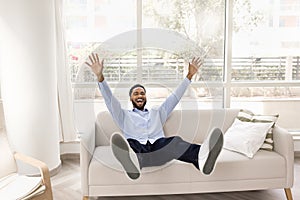 Joyful happy African man sitting on comfortable couch at home