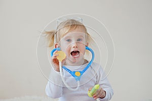 Joyful happy baby girl imagines as doctor at hospital using toy stethoscope and syringe.