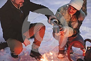 Joyful happy family couple in love basking by campfire outside in winter snowy forest