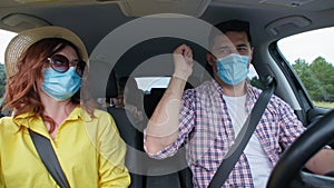 Joyful happy family have fun during joint trip by car on vacation observe safety precautions and wear medical masks to