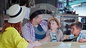 Joyful happy family of parents with children have fun at table in cafe and choose food and drinks from restaurant menu