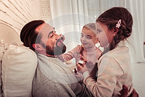 Joyful happy girls doing makeup for their dad