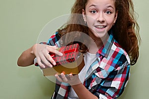 joyful, happy teenage girl in plaid shirt holds surprise gift box in her hands and opens it. Congratulations on holiday.