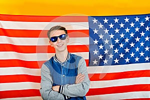 Joyful and happy teenager guy in sunglasses on a background of the American flag