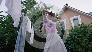 Joyful happy young woman in headphones listening to music dancing in slow motion outdoors. Clean laundry hanging on rope