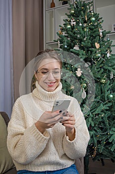 Joyful hipster girl in stylish glasses watching video on website via mobile phone