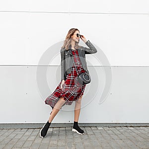 Joyful hipster woman in fashion sunglasses in fashionable casual beautiful red-black clothes in stylish sneakers with leather bag