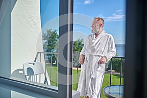 Joyful holidaymaker in the bathrobe basking in the sunlight