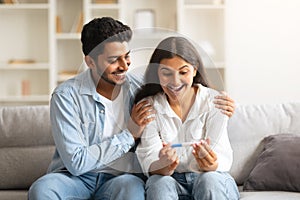 Joyful Indian couple with positive pregnancy test on sofa