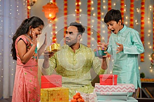 Joyful Indian father giving gift to sibling kids during diwali festive celebration at home - concept of happy childhood