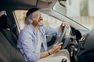 Joyful indian guy driving car, looking at rear view mirror