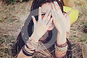 Joyful indie style woman with dreadlocks hairstyle, have a fun closing her face with a hands