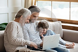 Joyful intergenerational family enjoying laptop app indoors.