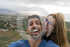 Joyful interracial Heterosexual Couple, Husband and Wife take a selfie looking at camera with affection, outside in honeymoon trip