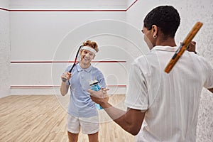 joyful interracial sportsmen with squash racquets