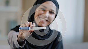 Joyful islamic young woman in hijab smiling happily holding pregnancy test excited pregnant lady surprised and happy