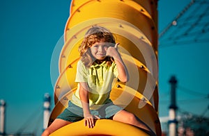 Joyful kid boy having fun on playground outdoors. Thumbs up. Happy blond kid boy having fun and sliding on outdoor