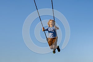 Joyful kid swinging on a swing. Happiness children. Child extreme swinging. Danger high Swing in sky. Craziness and photo