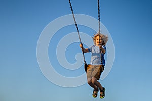 Joyful kid swinging on a swing. Happiness children. Child having fun on a swing outdoor. Craziness and freedom. Kid photo