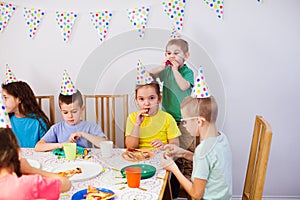 Joyful kids eating pizza at big table. Children wear birthday hats having fun together.