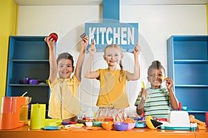 Joyful kids holding plastic tableware at toy kitchen.