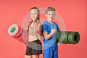 Joyful kids with sports equipment standing against red background