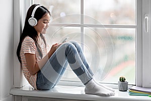 Joyful korean girl schooler playing games on cellphone, using headset