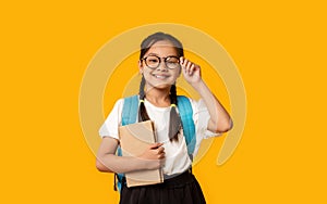 Joyful Korean Kid Girl Holding Book Posing Over Yellow Background