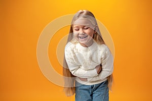 Joyful laughter of little blonde girl against yellow background in studio