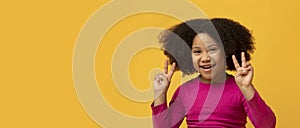 Joyful little afro girl gesturing peace sign and smiling at camera