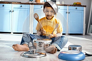 Joyful little boy playing on saucepan like a drummer