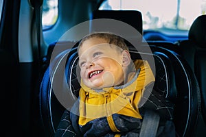 A joyful little boy smiles in a child`s car seat. Child safety when driving