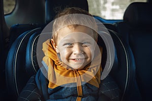 A joyful little boy smiles in a child`s car seat. Child safety when driving