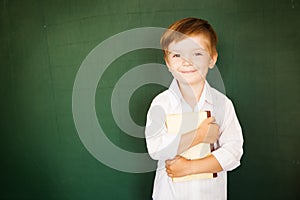 Joyful little boy standing on a blackboard background with a book in his hands. Free text, copy space