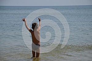 A joyful, little boy stands on the seashore in the water