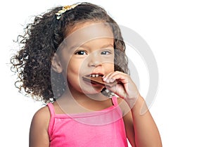 Joyful little girl with an afro hairstyle eating a chocolate bar