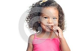 Joyful little girl with an afro hairstyle eating a chocolate bar