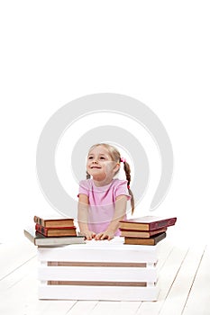 Joyful little girl with books sits on a white floor.